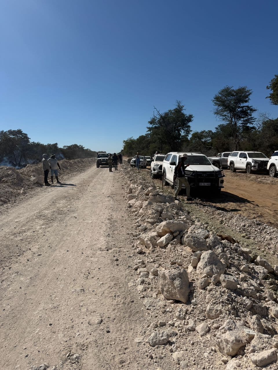 Vehicles and people gathered beside an unpaved work route